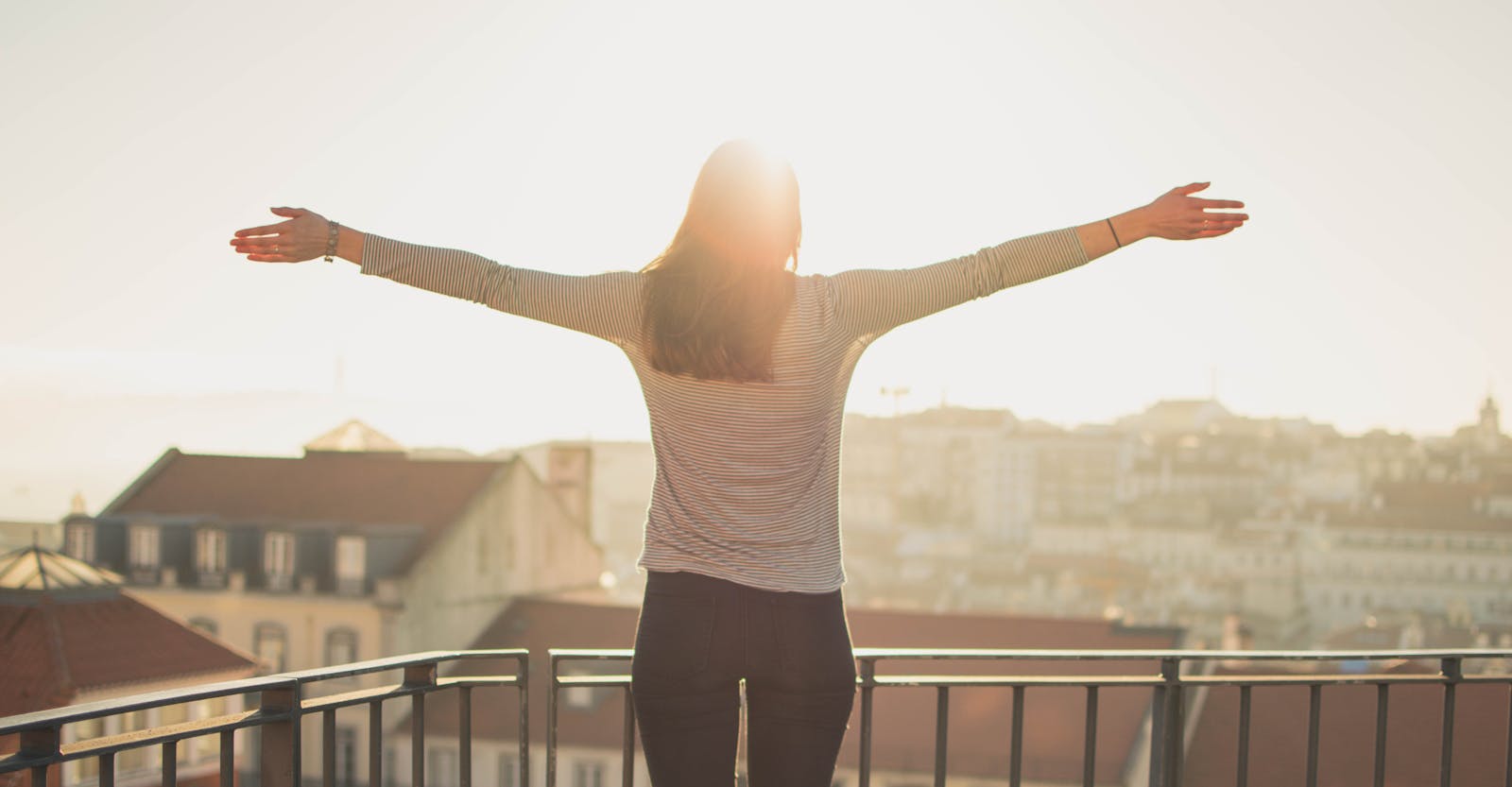 life A woman stands with outstretched arms on a sunny balcony, embracing the morning light.